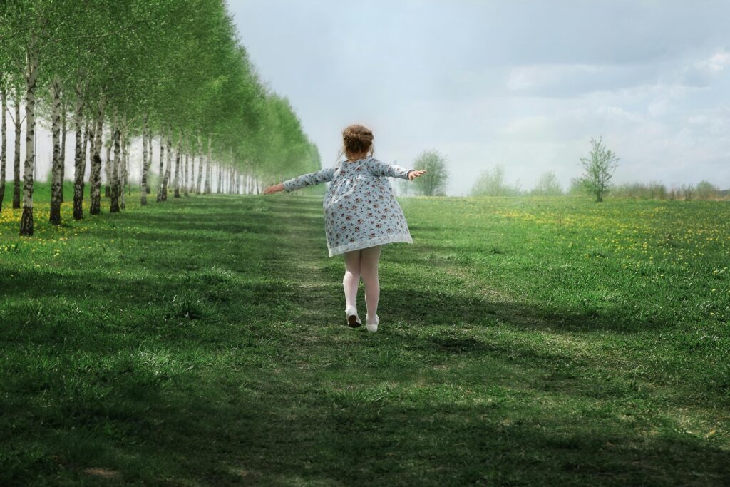 A child joyfully running down a tree-lined path in a lush green meadow on a sunny day.